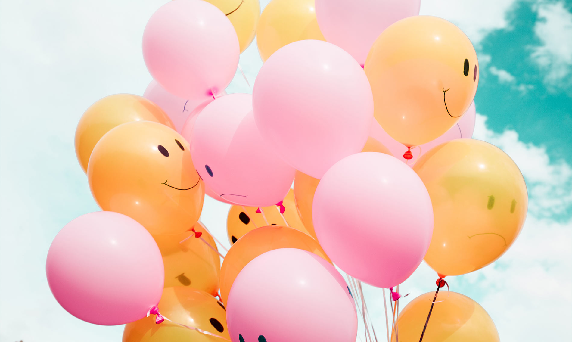 A photograph of a floating bunch of pink and orange balloons, some with happy faces on them and some with sad faces